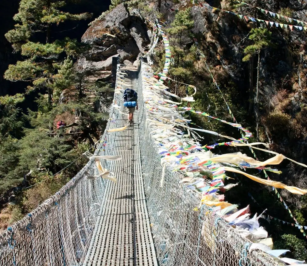 Trekker crossing a prayer-flag-lined suspension bridge over the Dudh Kosi