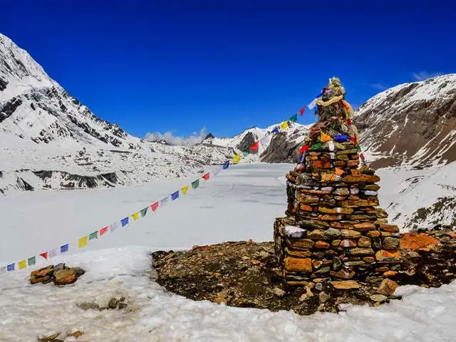 Stone cairn and prayer flags beside a frozen high-altitude lake