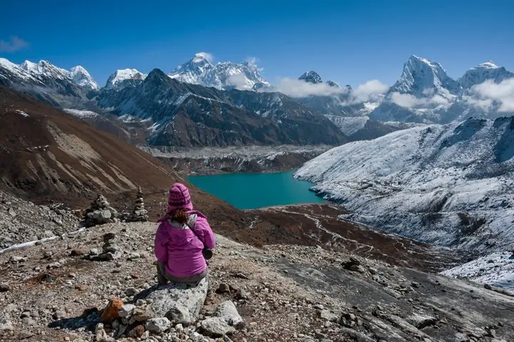 Trekker resting above Gokyo Lake with Everest and Cho Oyu beyond
