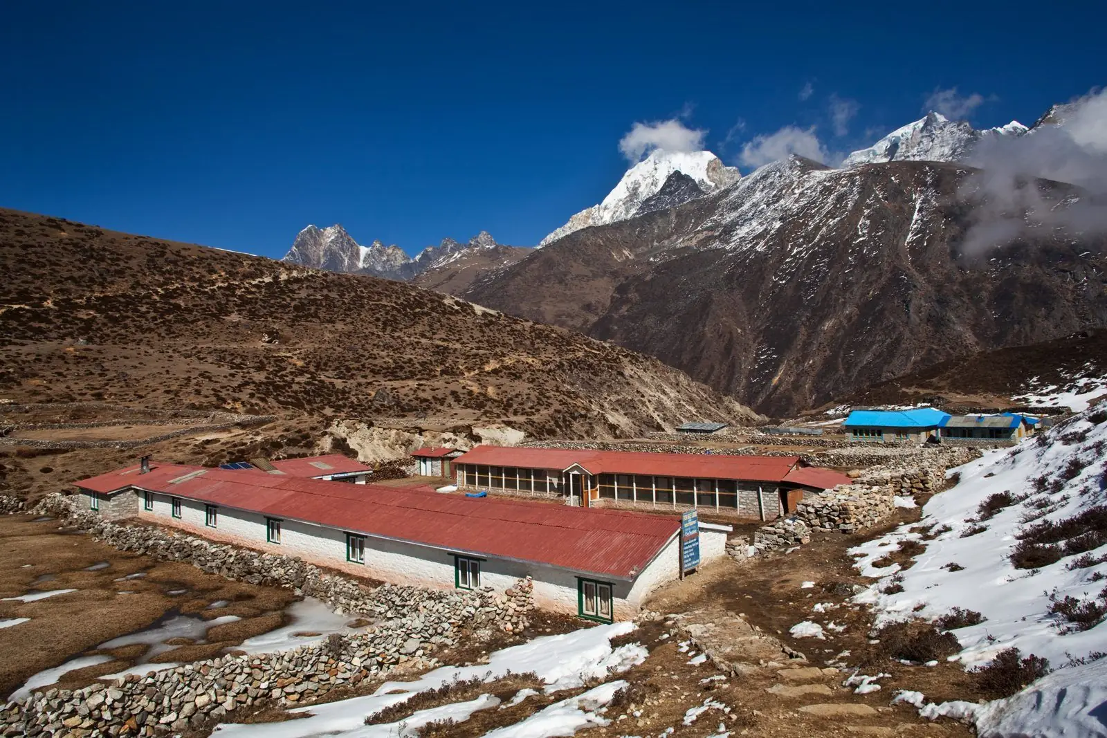 Red-roofed trekking lodges in a high valley with patches of snow