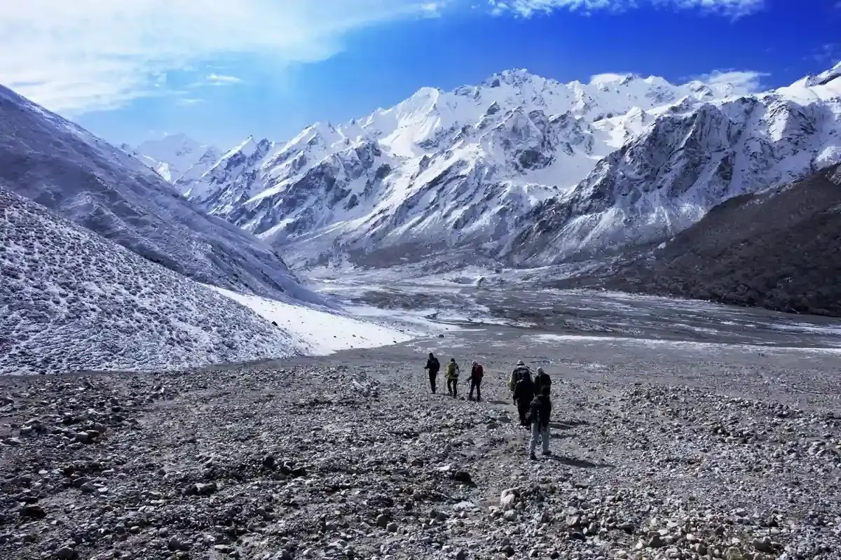 Small group of trekkers crossing a glacial moraine below snow peaks