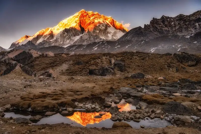 Peak glowing orange at sunset above a rocky valley with a reflection pool