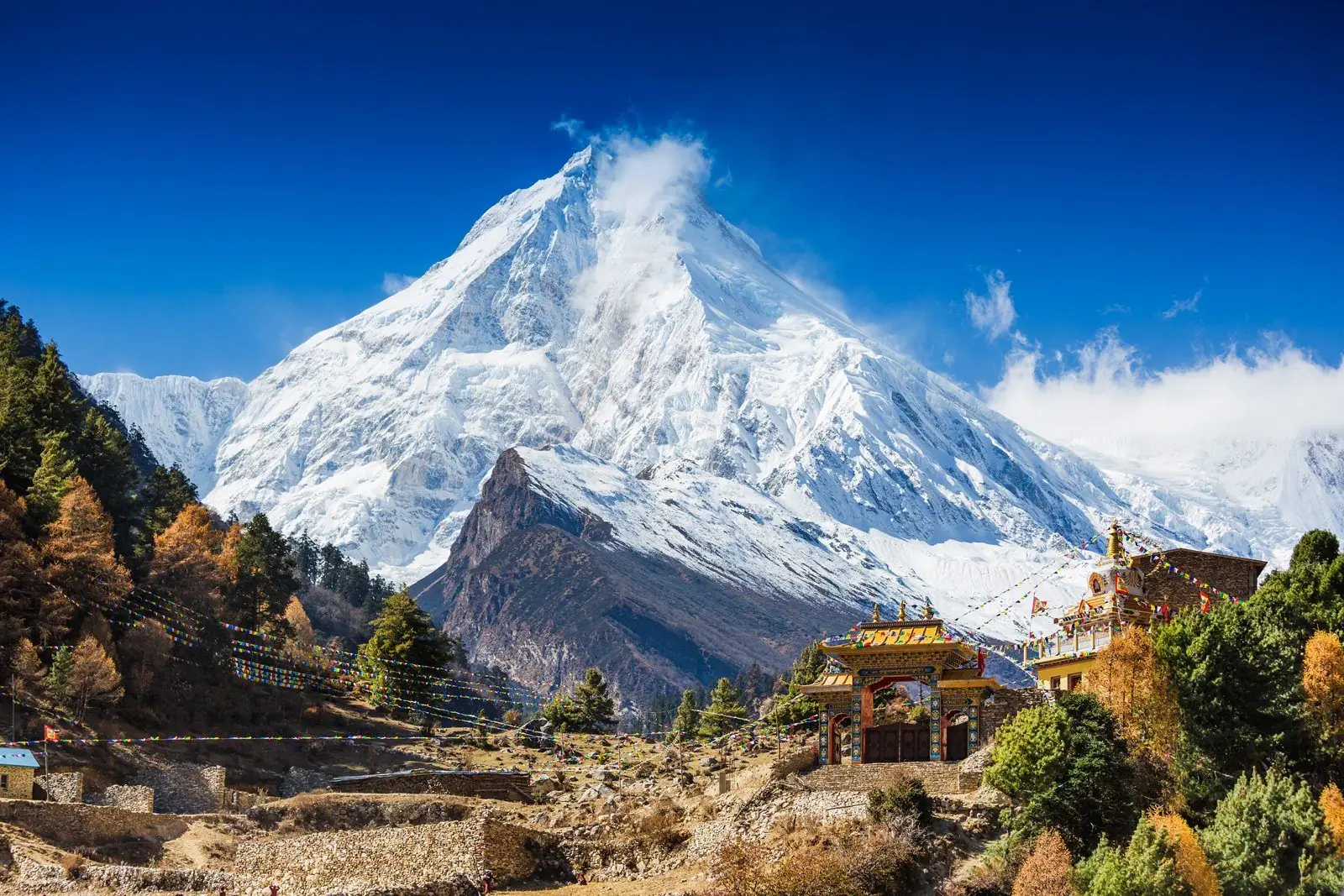 Monastery gate in autumn colours below a large snow peak in the Manaslu region