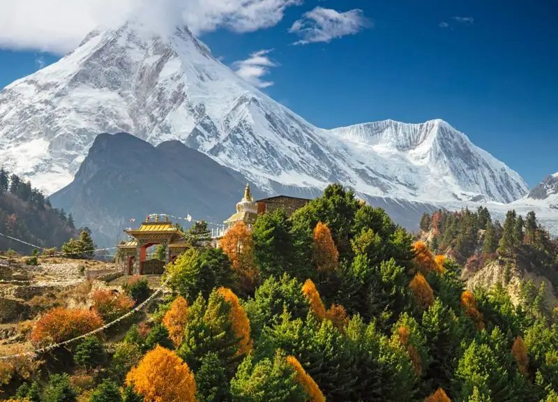 Snow-covered peak above a hillside monastery and autumn trees in the Manaslu region