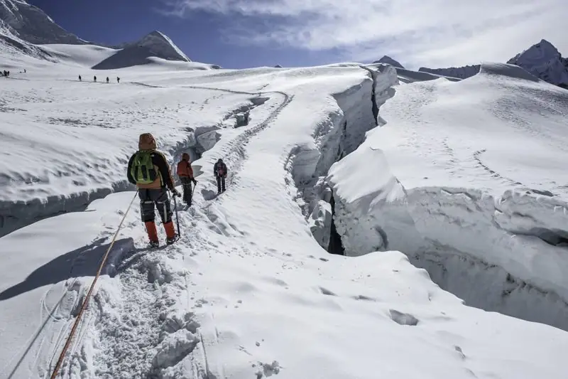 Roped climbers walking beside a crevasse on a glacier