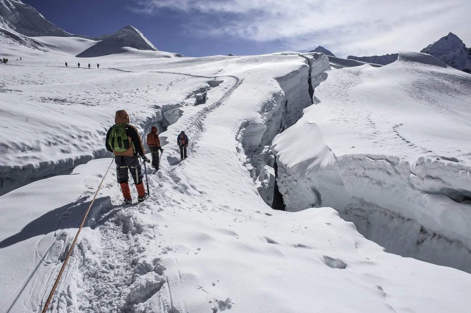 Roped climbers walking beside a crevasse on a glacier