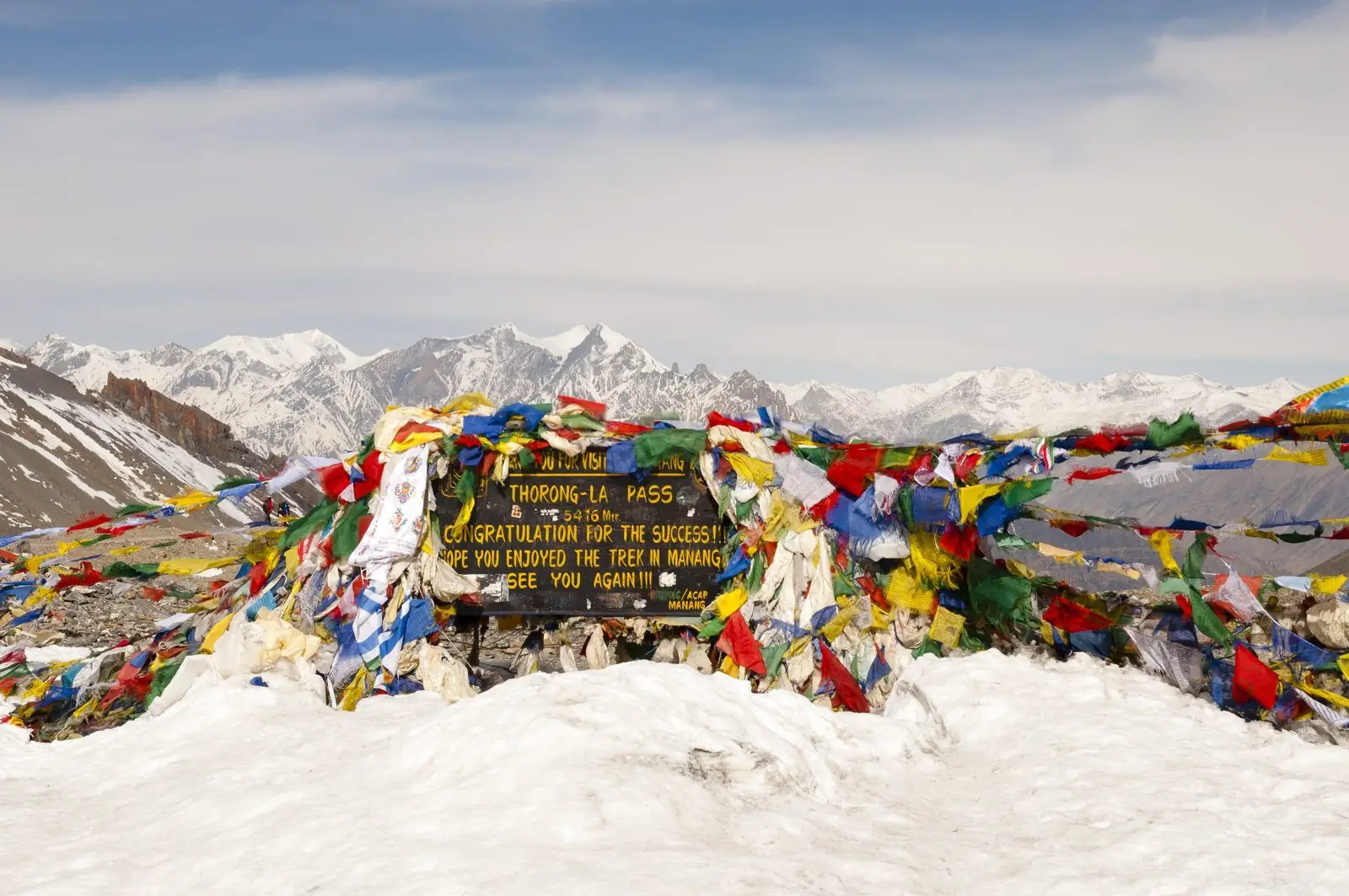 Prayer flags and a signboard at a high Himalayan pass in the snow